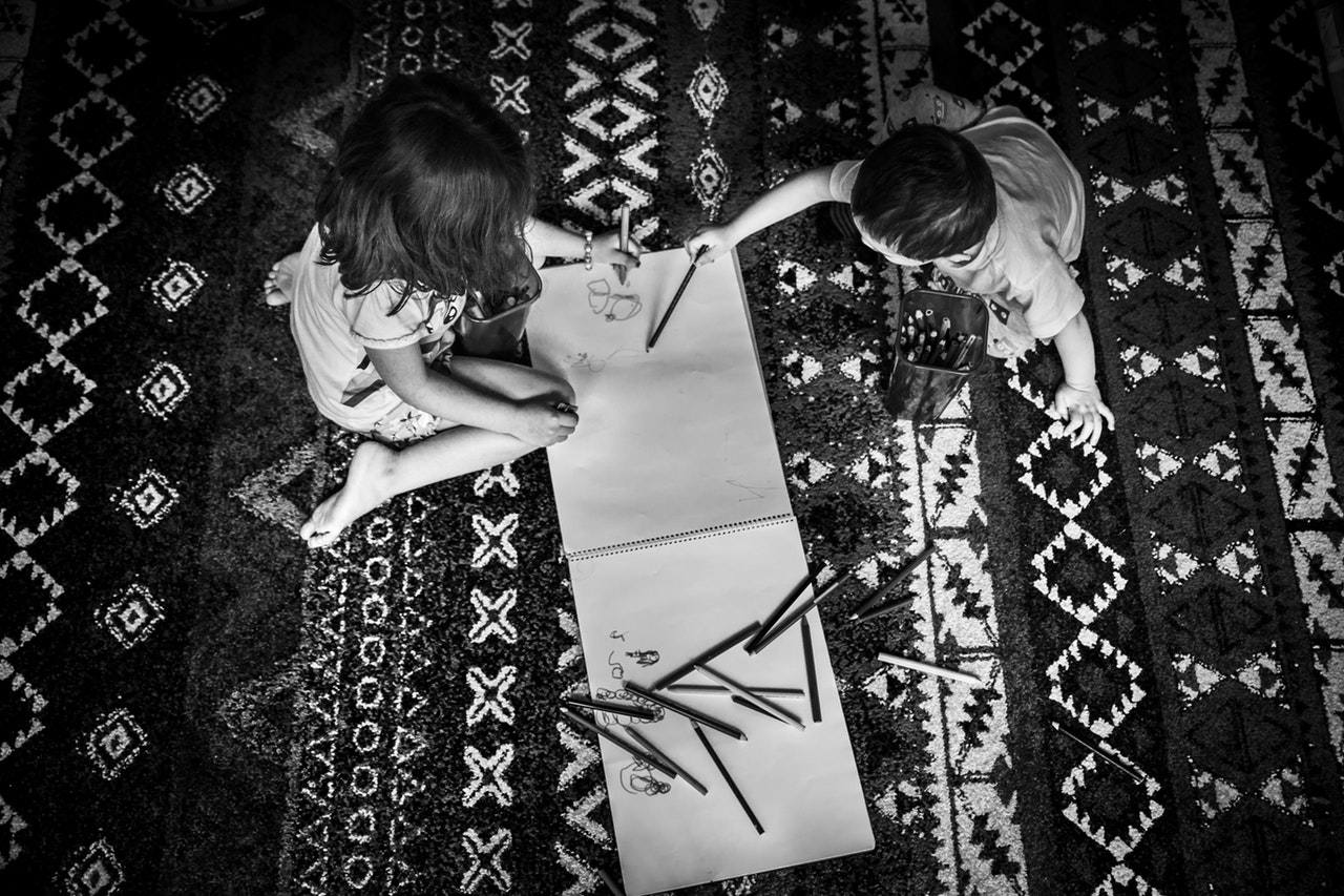 dzieci rysujące w bloku siedząc na wzorzystym dywanie