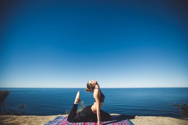 kobieta ćwicząca jogę na dywanie nad brzegiem morza